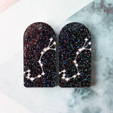 Pair of arch acrylic earrings with scorpio star constellation design in white again black glitter acrylic.
