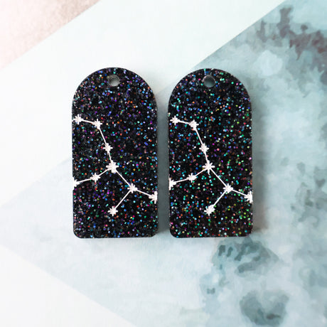 Pair of arch acrylic earrings with virgo star constellation design in white again black glitter acrylic.