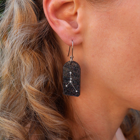 Close-up of an earring with a zodiac star design worn by a person with wavy hair.