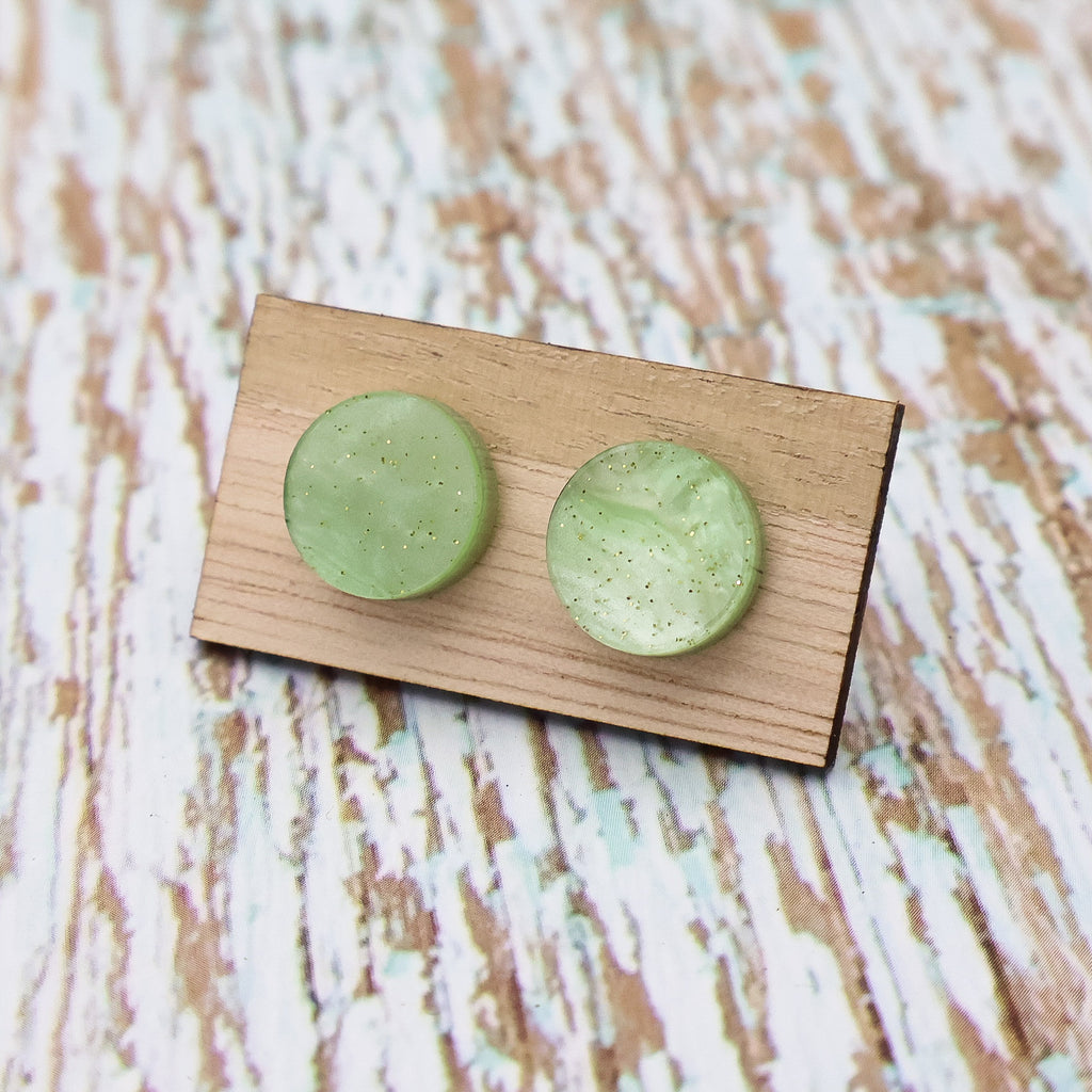 A pair of small apple green acrylic studs on a wooden backing card.