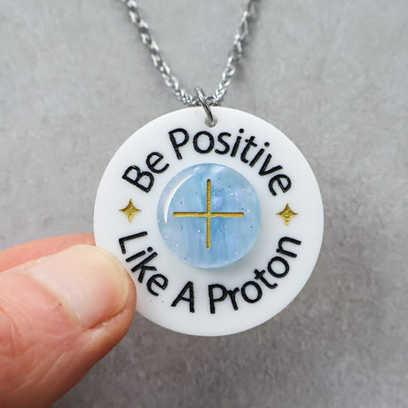 Necklace with a pendant that says 'Be Positive Like A Proton', being held up