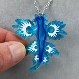 Blue and white sea dragon pendant on a chain held by a hand against a gray background