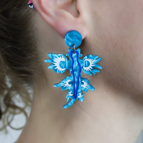 Laser cut acrylic blue sea dragon earrings, being modelled.