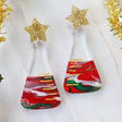 A pair of dangle earrings featuring a conical flask design with Christmas-themed decorations, including red and green swirls and gold accents, topped with glittery star-shaped acrylics.