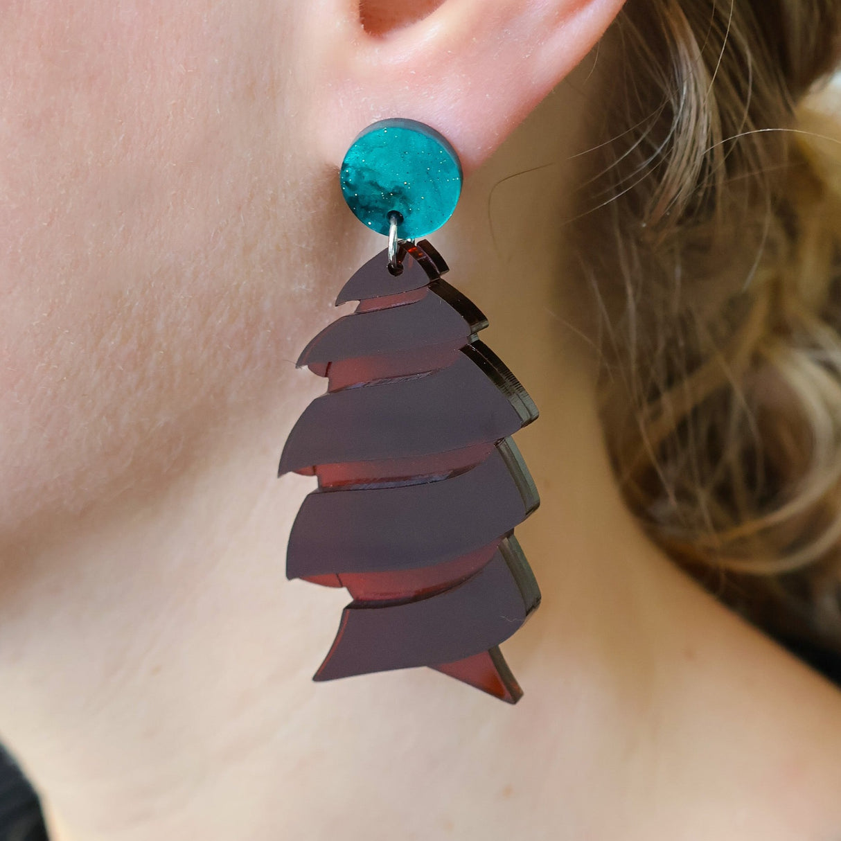 Brown acrylic cork screw shark egg earrings being modelled, showing green acrylic toppers and transparency in the broch acrylic. 