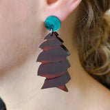 Brown acrylic cork screw shark egg earrings being modelled, showing green acrylic toppers and transparency in the broch acrylic. 
