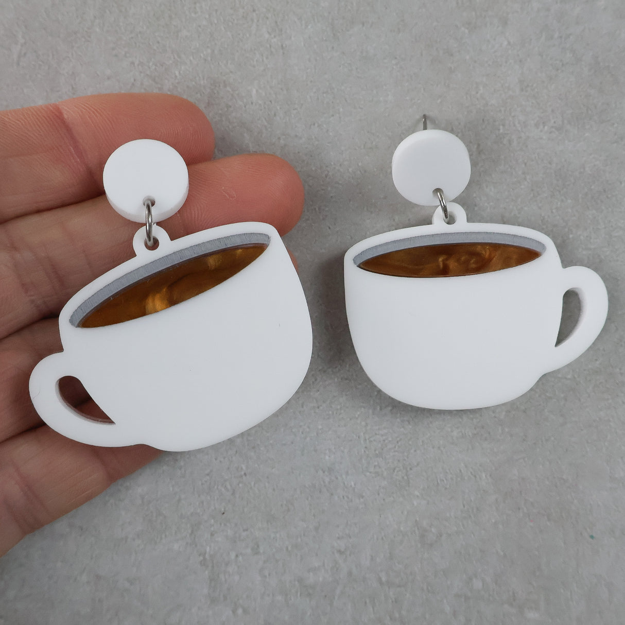 White cup-shaped earrings with a brown center held by a hand on a gray background