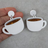 White cup-shaped earrings with a brown center held by a hand on a gray background