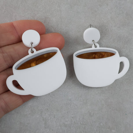 White cup-shaped earrings with a brown center held by a hand on a gray background