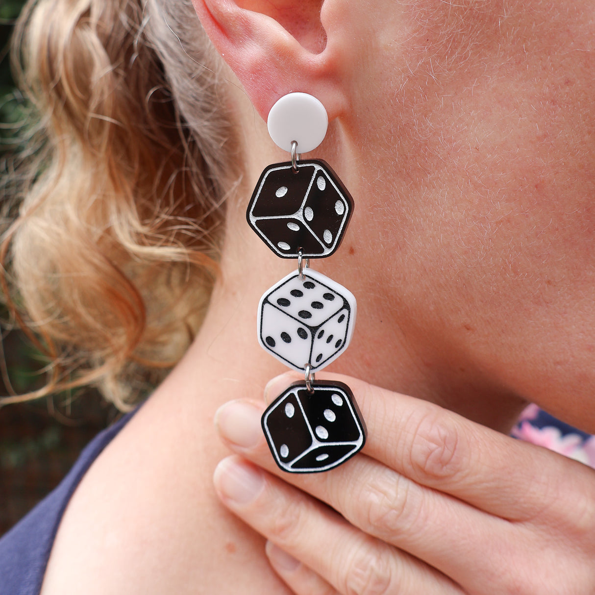 Close-up of a person wearing black and white dice-shaped earrings. 3 dice hang from a round earring topper.