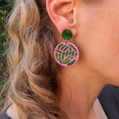 Close-up of a person wearing pink and green e.coli acrylic earrings. 