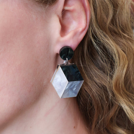 Small greyscale laser cut acrylic cube earrings being modelled.