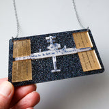 Acrylic Space station necklace held by a hand against a white background