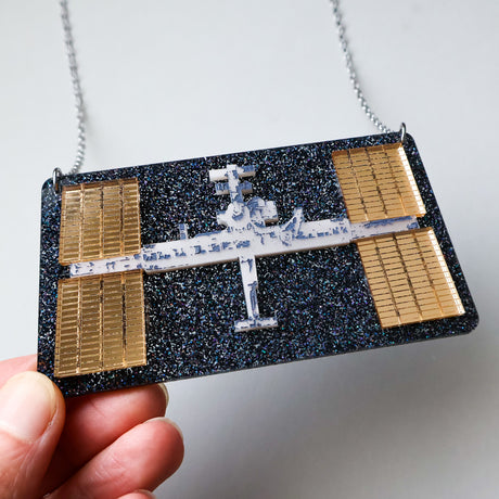 Acrylic Space station necklace held by a hand against a white background