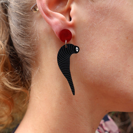 Close-up of a person wearing a black leech acrylic earring hanging from a red topper. 