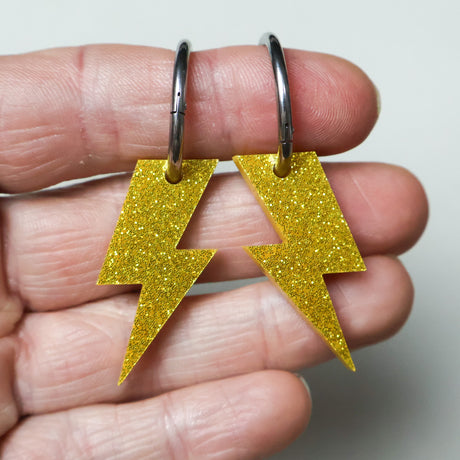 closeup view of yellow glitter lightening bold earrings on huggie hoops. 