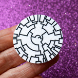 A round black and white acrylic brooch depicting a phylogenetic tree being held in a hand. 