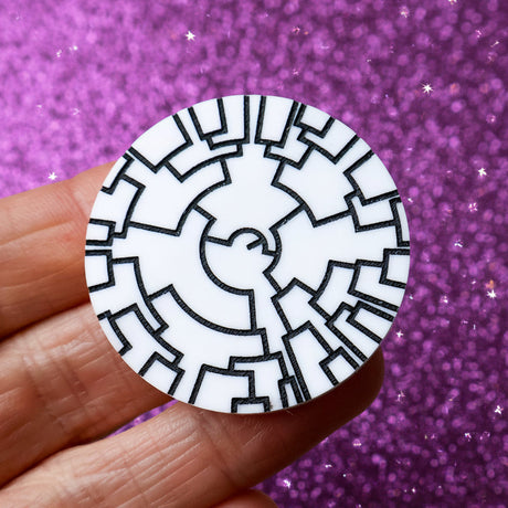 A round black and white acrylic brooch depicting a phylogenetic tree being held in a hand. 