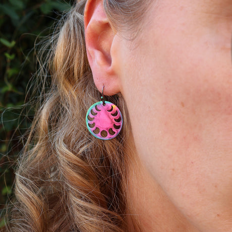 Close-up of a person wearing colourful stainless steel moon phase earrings.