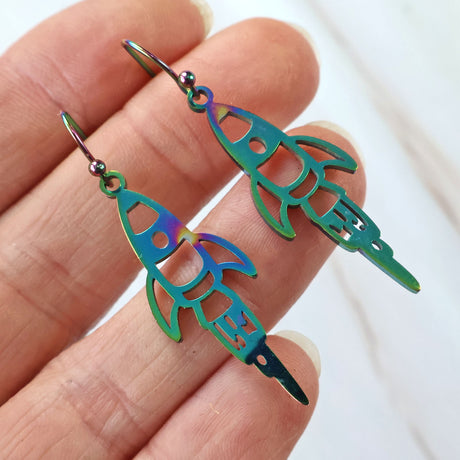 A pair of rainbow rocket earrings with stainless steel french hooks, held in a person's hand.
