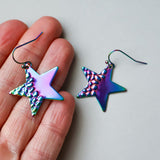 Star-shaped earrings with a metallic, iridescent finish held between fingers on a light background.
