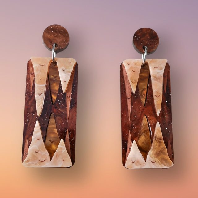 A pair of acrylic earrings displaying stalactite and stalagmites, made from brown and gold toned acrylics.