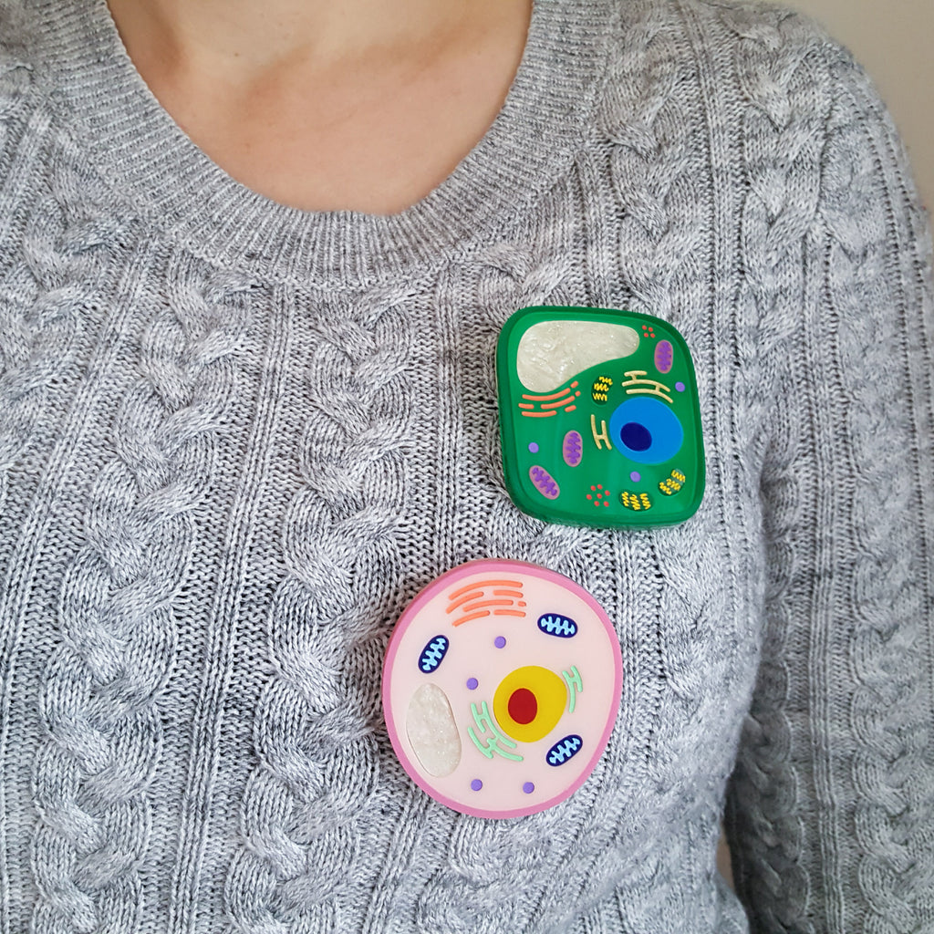 Plant and animal cell acrylic brooches being worn on a cable knit grey sweater.