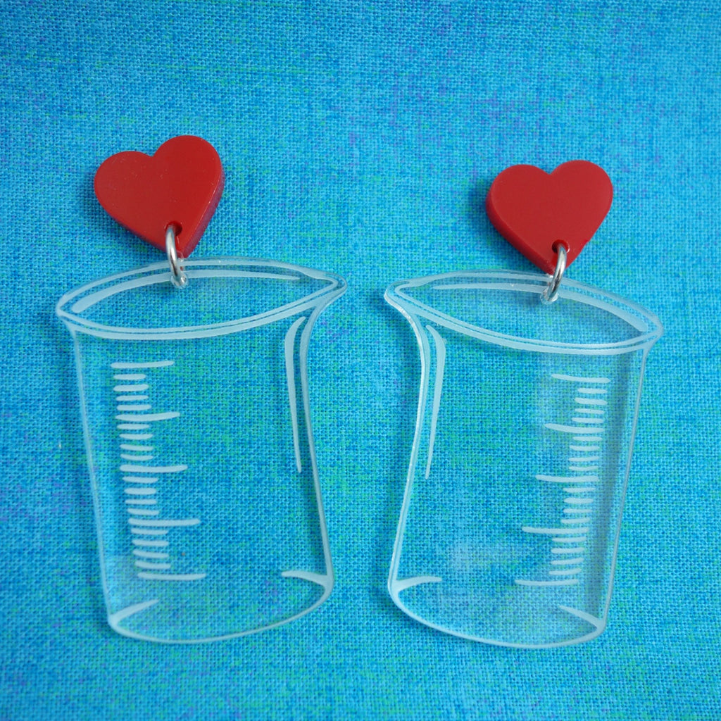 Laser Cut Acrylic Clear Beaker Earrings with Red Heart Earring Toppers. Chemistry Glassware Earrings. Blue background.