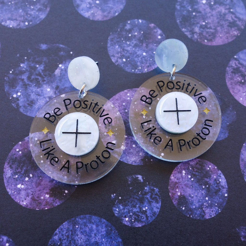 Laser cut earrings with the text 'Be Positive Like a Proton.'