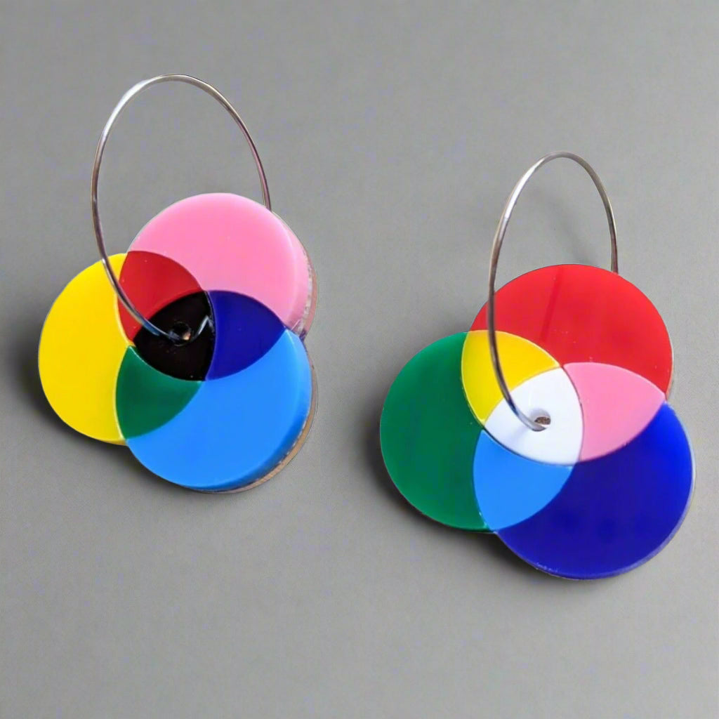 Asymmetrical Laser Cut Acrylic Colour Wheel Earrings showing additive and subtractive colour diagrams. Earrings are sitting on a concrete surface.
