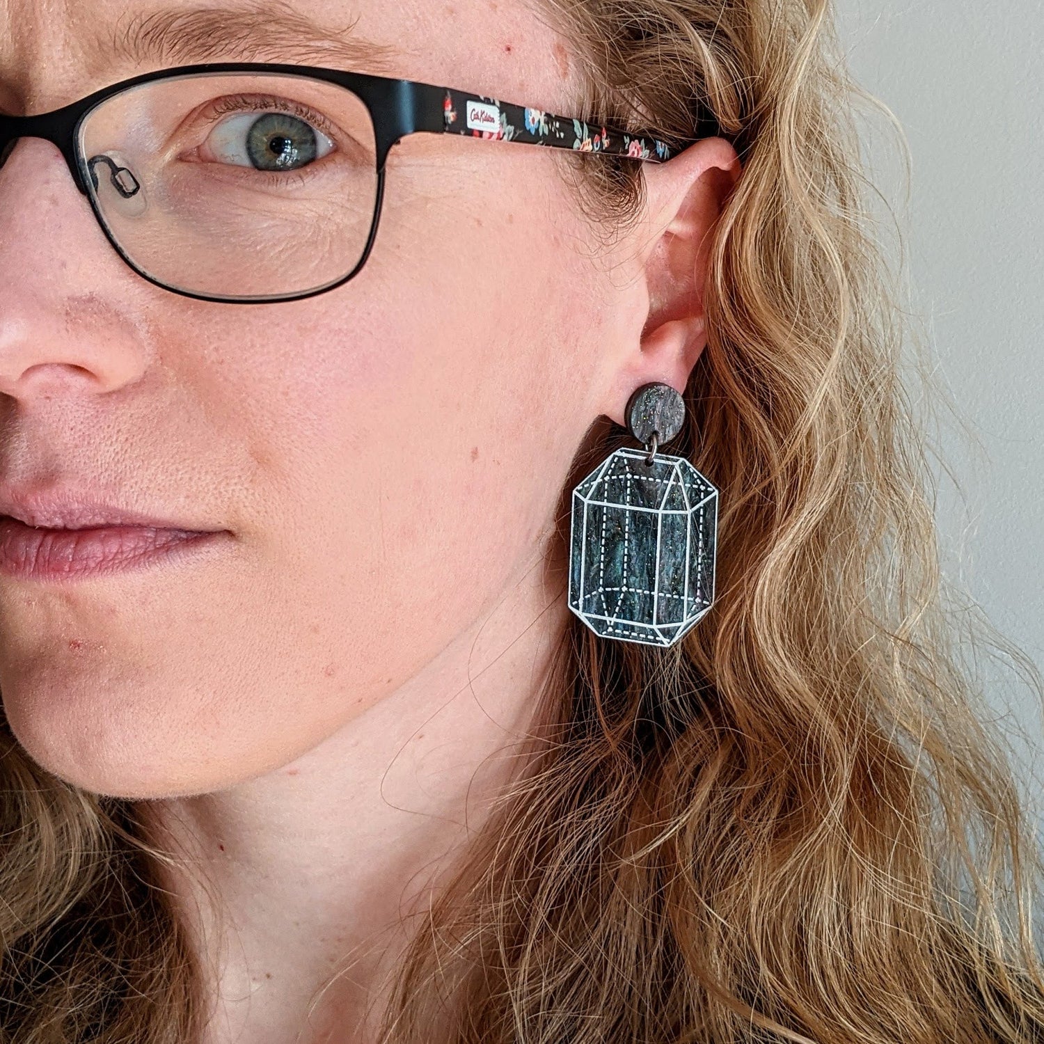 Laser cut crystal design earrings in galactic dark glittery acrylic being modelled.