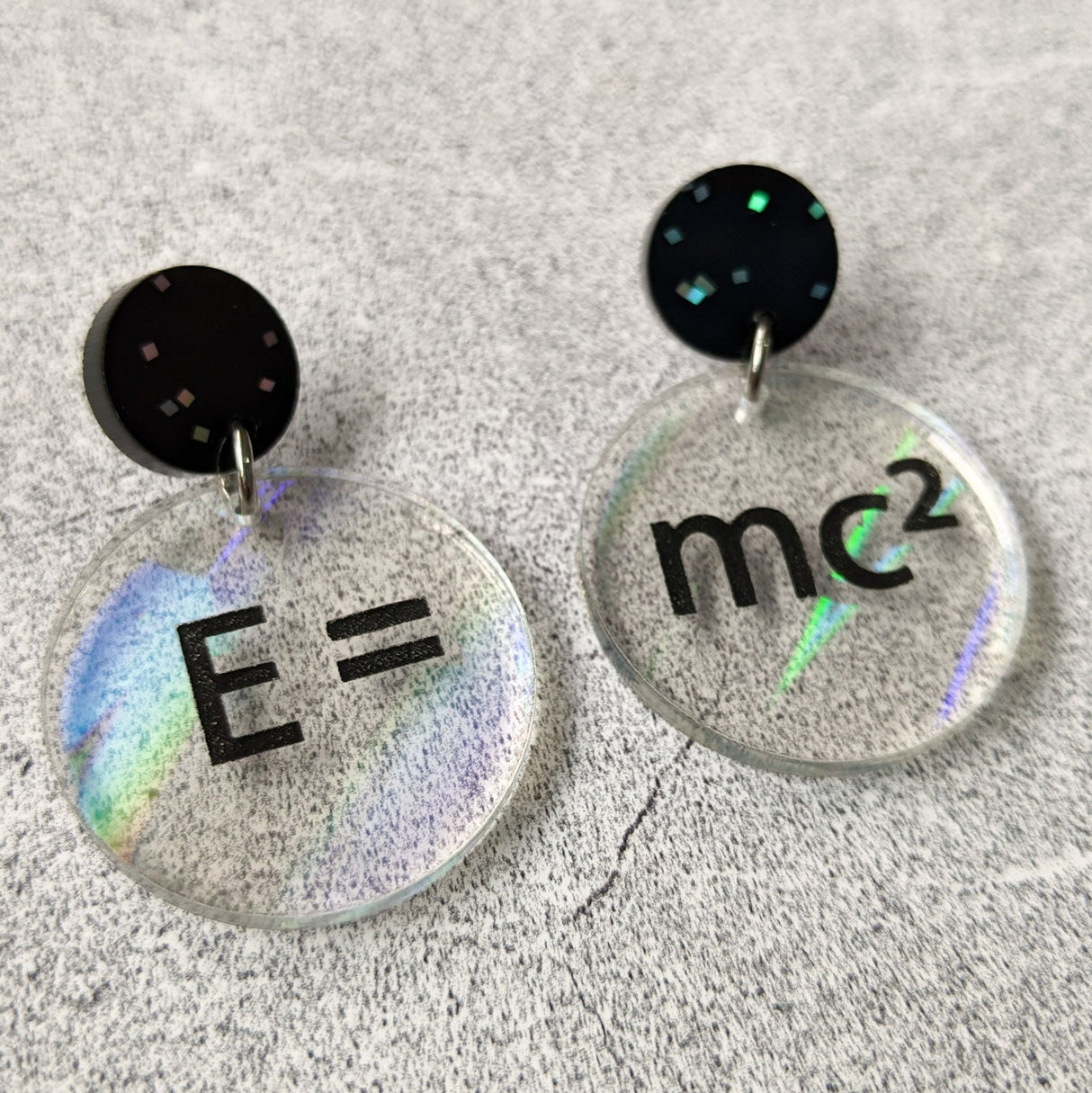 E =mc2 earrings, with black text engraved into holographic effect acrylic discs. Equation bridges both earrings. Black glitter earring toppers. Alternative view.