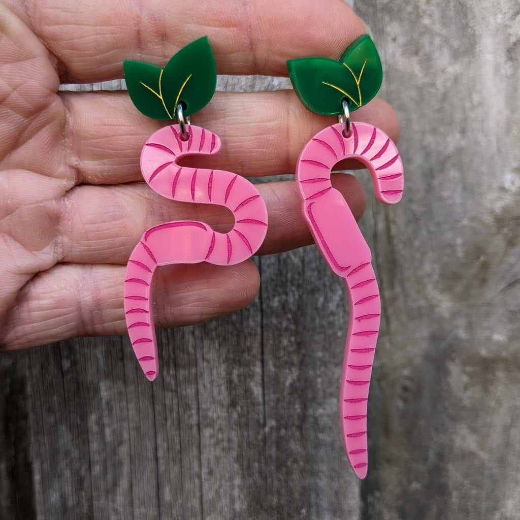 Pink Acrylic Asymmetrical Earth Worm Earrings hanging from Green Leaf Toppers. 