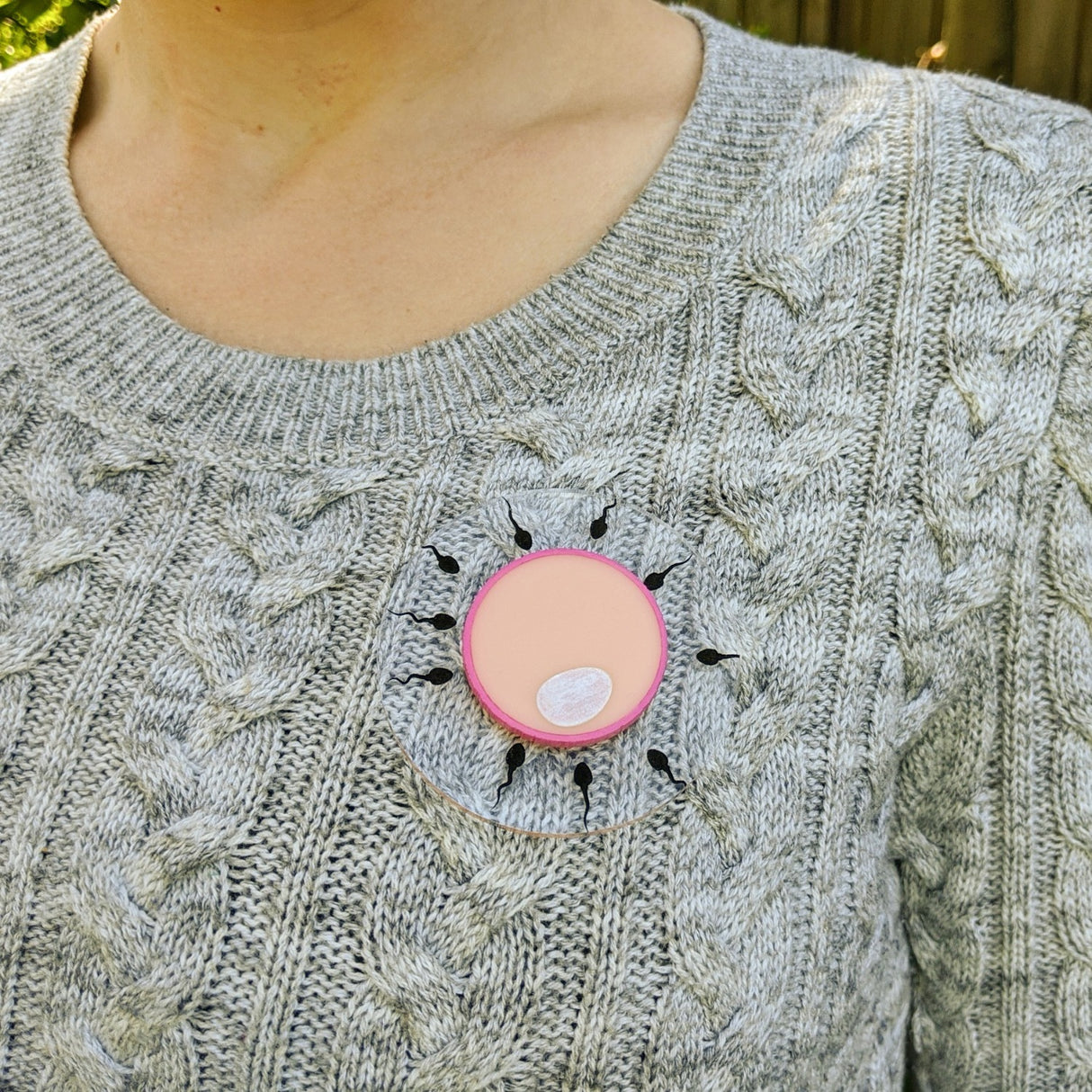 Acrylic Human Egg and Sperm cell Brooch being modelled by a woman in a grey sweater