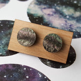 A pair of small acrylic studs on a wooden backing card.