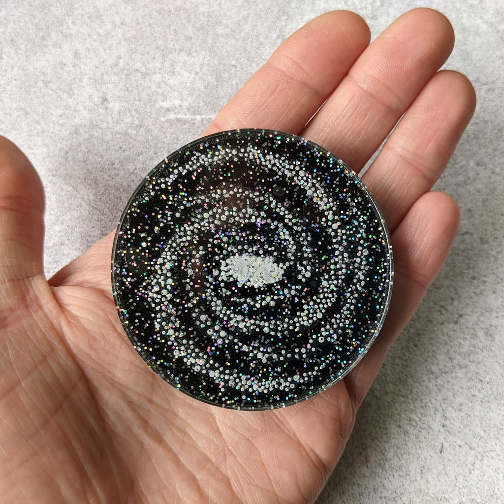 Laser Cut Acrylic Milky Way Galaxy Brooch 60mm diameter disc. Black with Glittery Stars. Held in hand. 