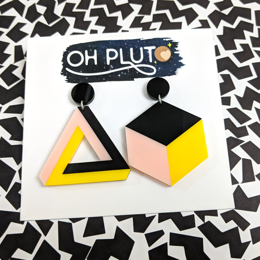 Asymmetrical geometric earrings, comprising of a statement sized cube and triangle in black, pink and yellow toned laser cut acrylics.