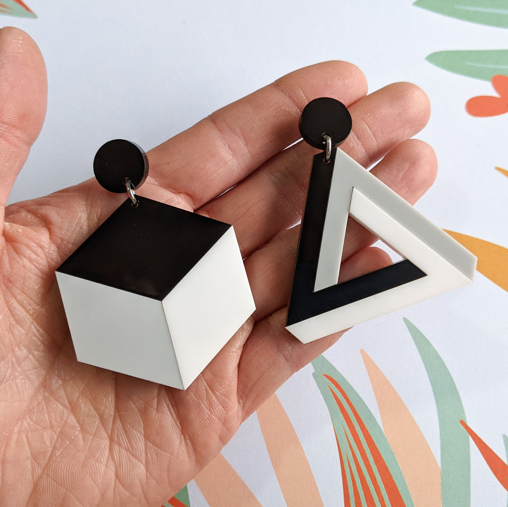 Asymmetrical geometric earrings, comprising of a statement sized cube and triangle in black, white and grey laser cut acrylics.