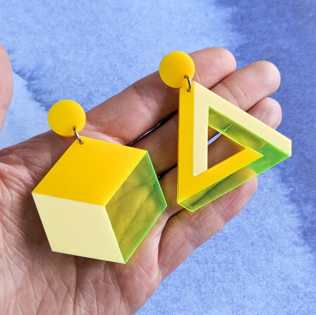Asymmetrical geometric earrings, comprising of a statement sized cube and triangle in three different yellow toned laser cut acrylics.