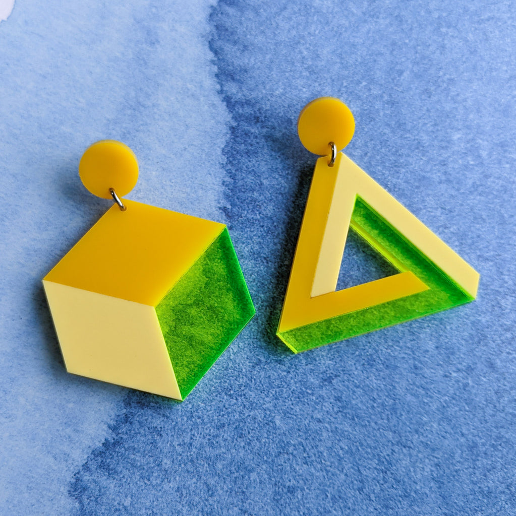 Asymmetrical geometric earrings, comprising of a statement sized cube and triangle in three different yellow toned laser cut acrylics.