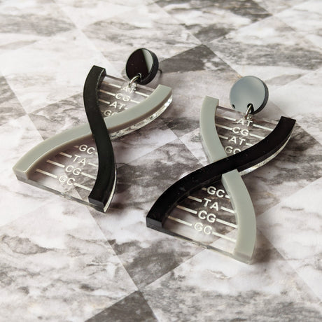 A pair of DNA earrings in greyscale, handmade from laser cut acrylic.