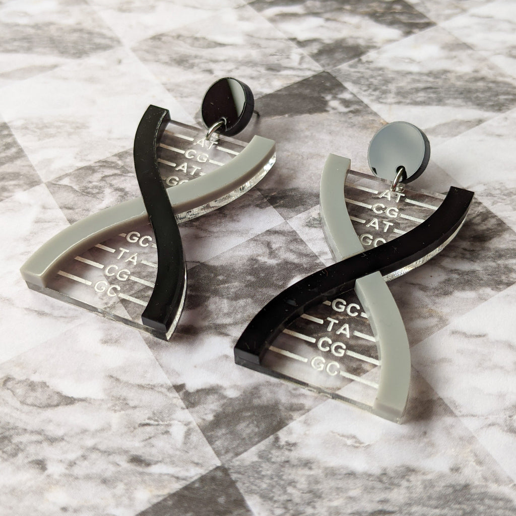 A pair of DNA earrings in greyscale, handmade from laser cut acrylic.