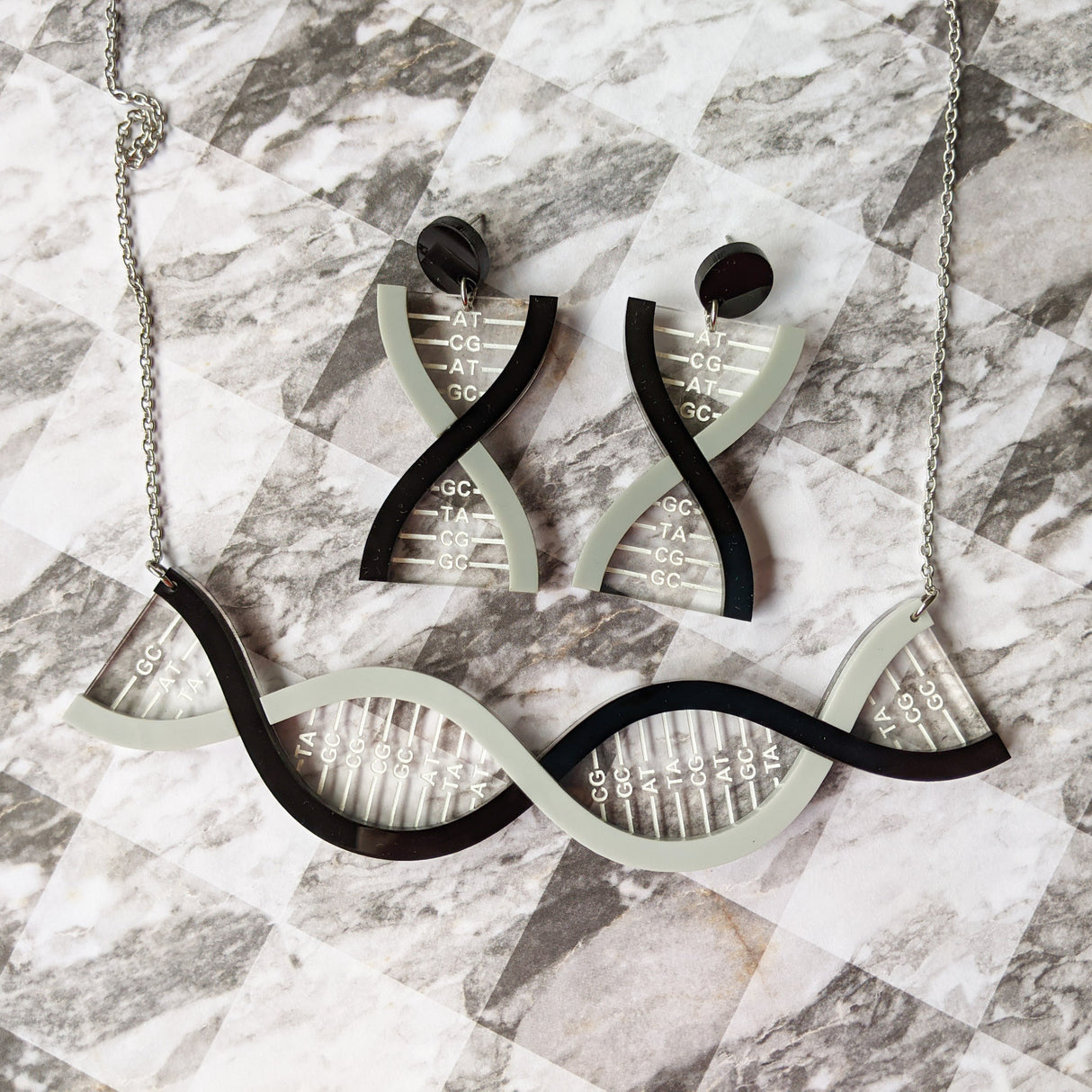 A DNA necklace and a matching pair of DNA earrings, in greyscale, handmade from laser cut acrylic.