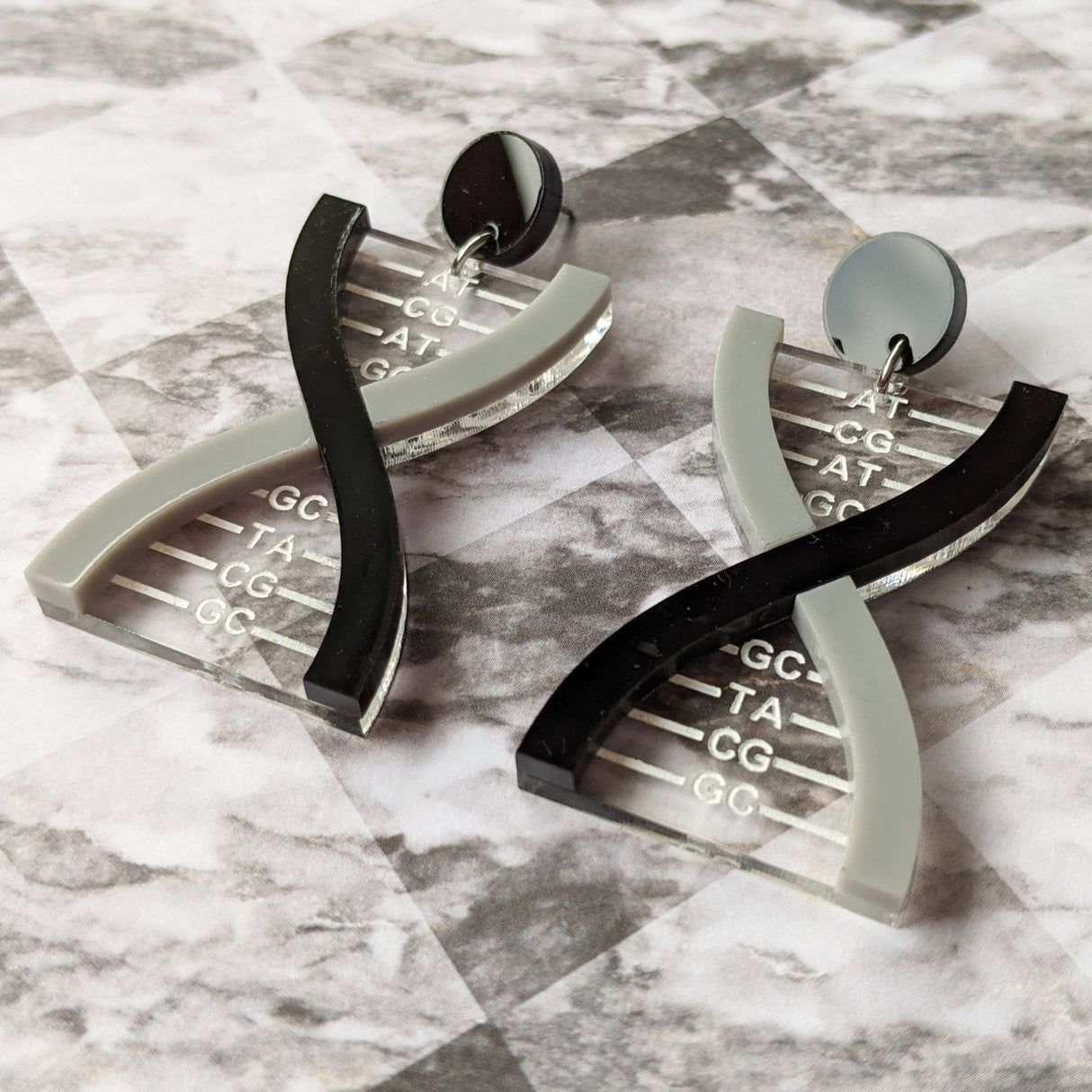 A pair of DNA earrings in greyscale, handmade from laser cut acrylic.