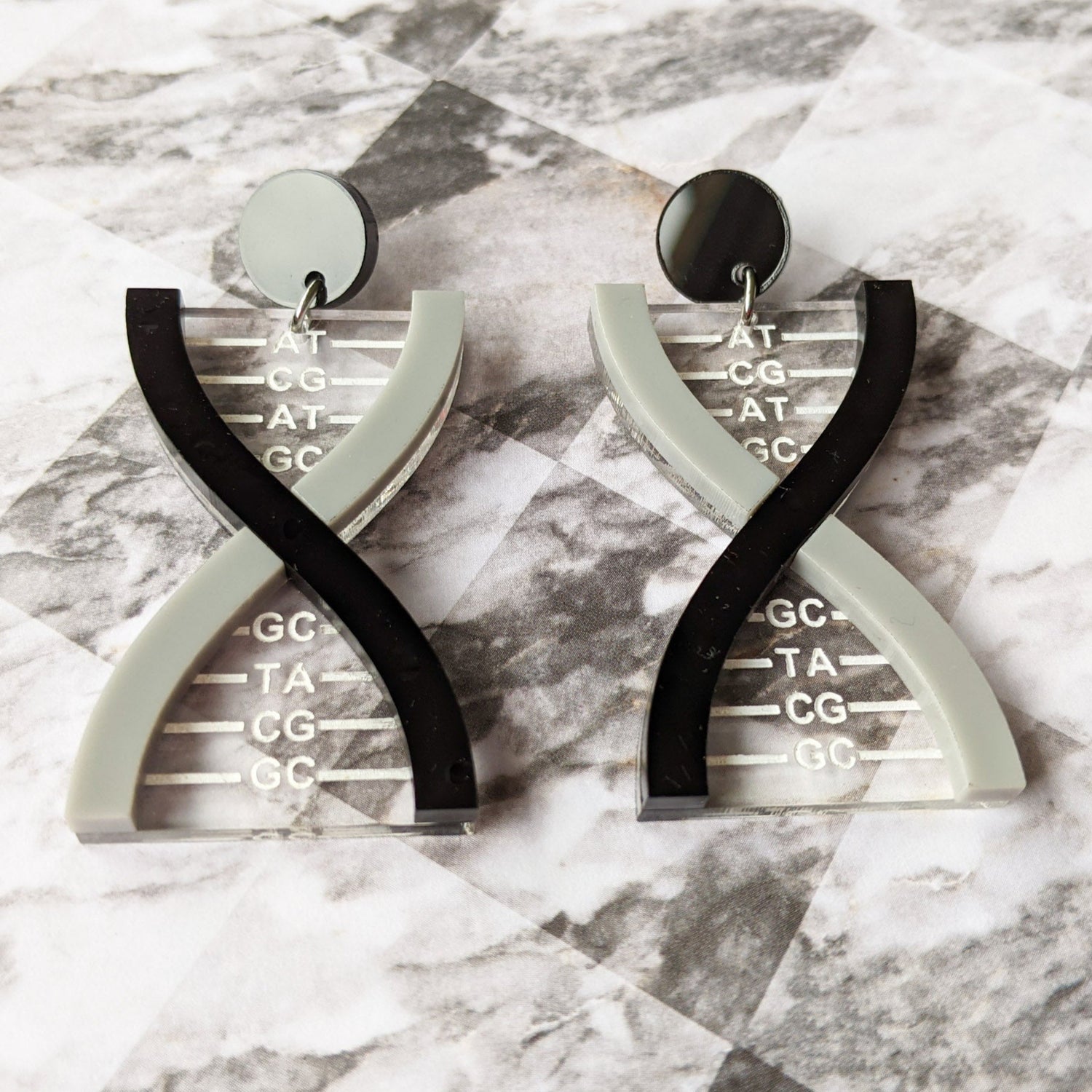 front view of a pair of DNA earrings in greyscale, handmade from laser cut acrylic.