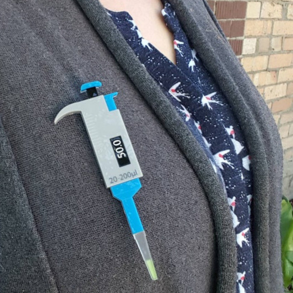 Acrylic micropipette brooch being modelled against a grey cardigan.