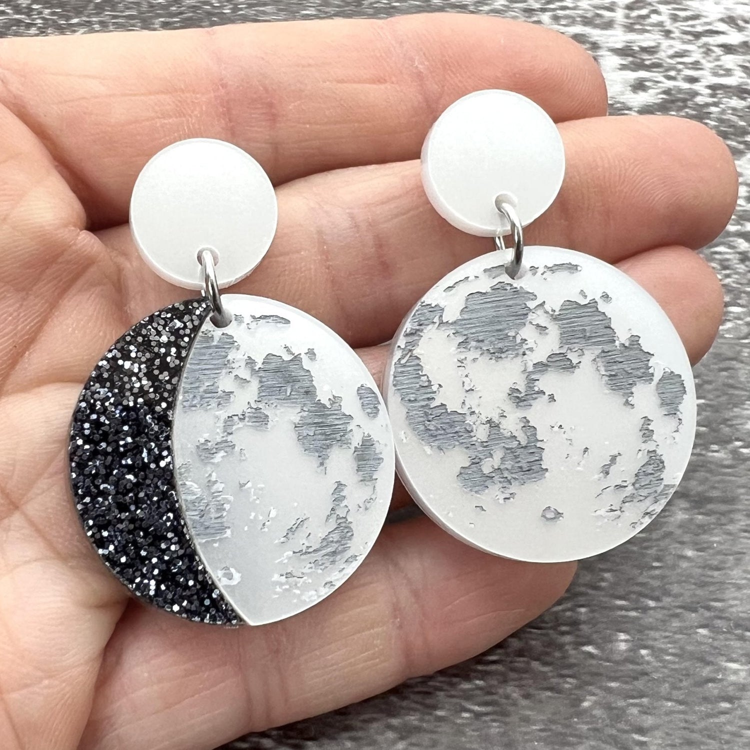 A pair of asymmetrical moon phase earrings, laser cut from pearlescent toned acrylic.