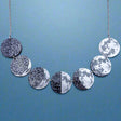 A laser cut acrylic moon phase necklace, showing the transition of the moon from new to full. Front view.