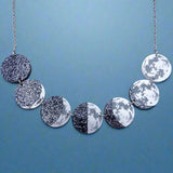 A laser cut acrylic moon phase necklace, showing the transition of the moon from new to full. Front view.