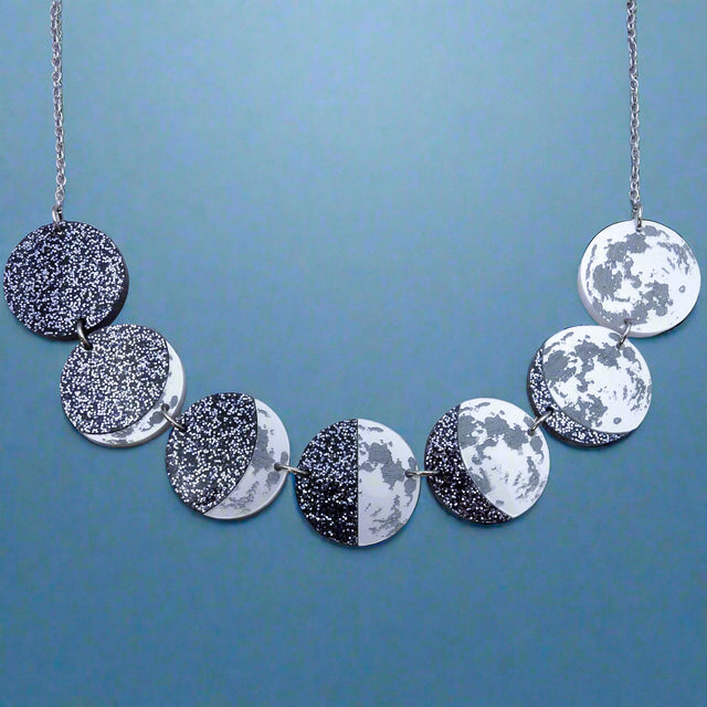 A laser cut acrylic moon phase necklace, showing the transition of the moon from new to full. Front view.